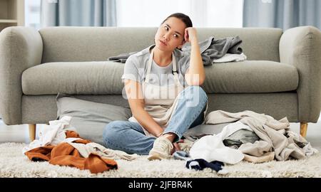 A young mixed race domestic cleaner looking distracted and overwhelmed while folding laundry. A beautiful Asian woman daydreaming while doing Stock Photo