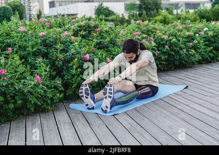 Fit man with physical disability doing warm-up stretching before exercise routine outdoor - Focus on leg prosthesis Stock Photo