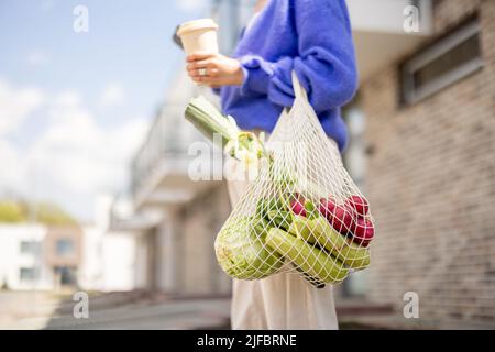 Woman with mesh bag full of vegetables and reusable coffee cup outdoors Stock Photo