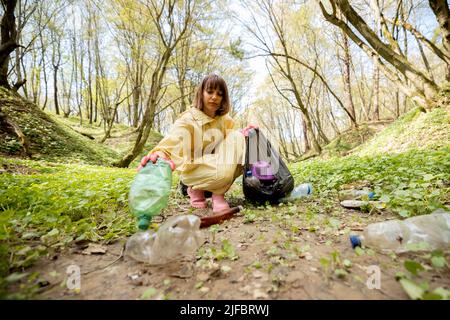 Woman collecting scattered plastic garbage in the woods Stock Photo