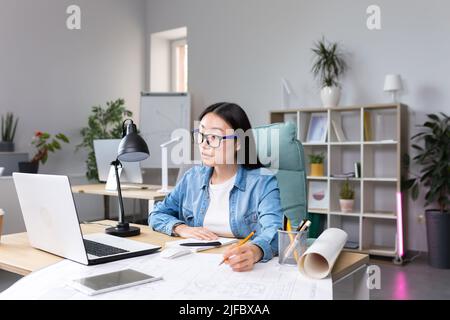 Asian designer working in office, with blueprints, woman at work in casual clothes. Stock Photo