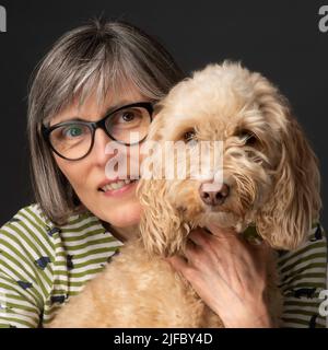 Studio portrait of a blonde Cockapoo dog with middle aged caucasian female with grey hair. Stock Photo