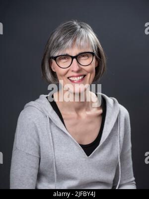 Grey-haired, middle-aged caucasian female, wearing glasses, looking at the camera, smiling. Stock Photo