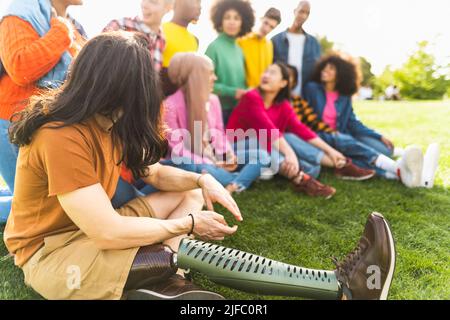Close up view of young man with prosthetic leg having fun with a group of multiracial friends in park outdoor - Friendship and diversity concept Stock Photo