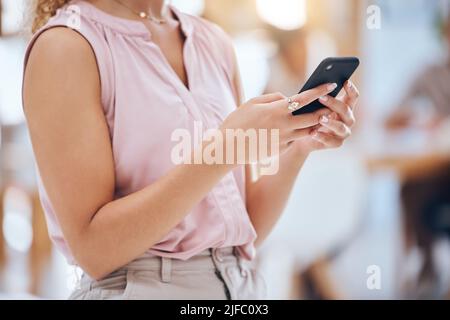 Closeup cropped view of a unrecognizable mixed race businesswoman stand alone and sending a text using her smartphone in the office at work. Female Stock Photo