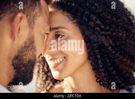 Closeup of an young affectionate mixed race couple standing on the beach and smiling during sunset outdoors. Hispanic couple showing love and Stock Photo