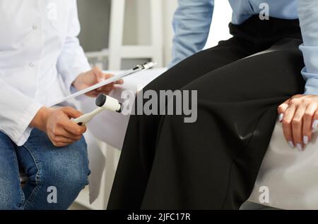 Hammer in hand of neurologist doctor next to legs of patient seated on hospital couch Stock Photo