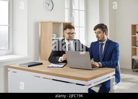 Two businessmen working together on one profitable project sitting at same laptop. Stock Photo