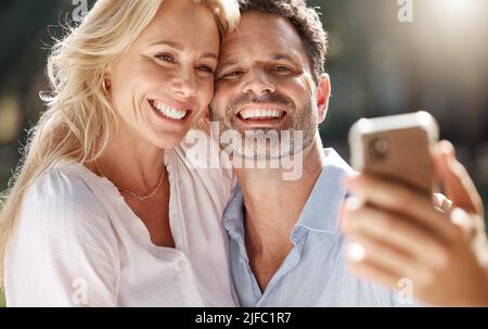 Closeup of a happy mature couple taking a selfie outside in the backyard using a smartphone on a sunny day. Stock Photo
