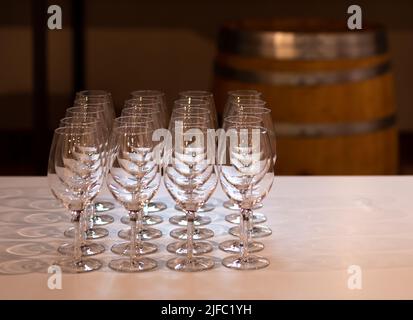 sparkling crystal wine glasses arranged in a row on a table with a white tablecloth ready for wine tasting, matrix, wine barrel in background Stock Photo