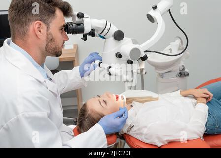 Male dentist working with dental microscope. Open female mouth during oral checkup at the dentist Stock Photo
