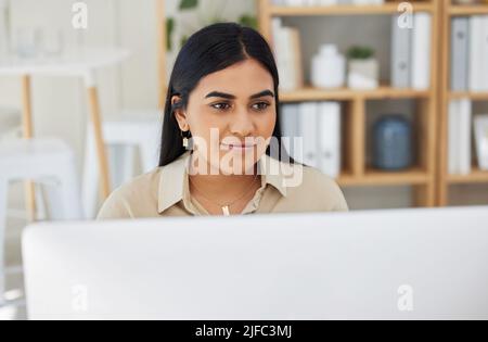 One beautiful young mixed race business woman working on her computer in the office at work. Confident and successful female entrepreneur of indian Stock Photo
