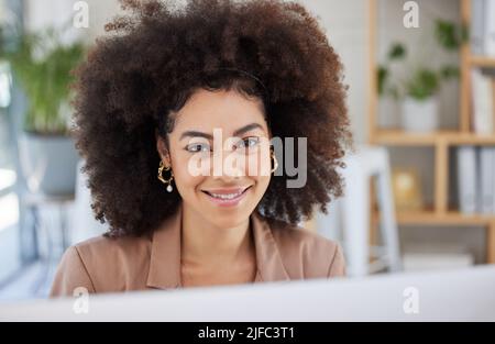 Young happy confident mixed race businesswoman smiling while using a desktop computer working in an office. One hispanic businesswoman with a curly Stock Photo