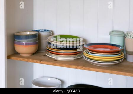 Wooden shelf with kitchen utensils, rustic style. Tableware, plates and bowls stand on a shelf in the kitchen. Cupboard with set of colourful dishes, Stock Photo