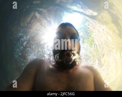 A bearded man in swimming goggles blows bubbles underwater. Blurred image Stock Photo
