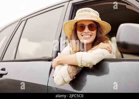 Portrait of One beautiful young brunette caucasian woman hanging out the window of a car while taking a road trip, travelling to her destination Stock Photo