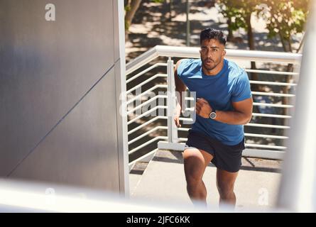 Handsome mixed race athletic man running up the steps on of a building while focused on his fitness. Hispanic male serious about his health while Stock Photo