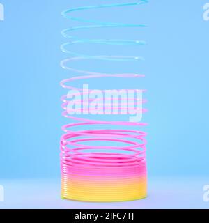 Spiral slinky toy isolated against a blue background. Closeup of a colourful retro plastic toy stretching, twirling and coiling. Spring toy for Stock Photo