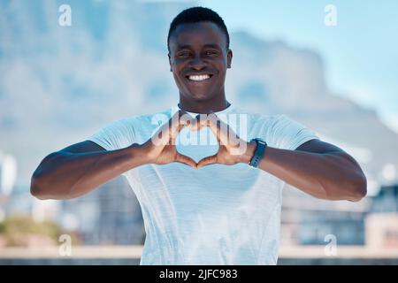 Portrait of one smiling muscular african american man outside alone and using hand gestures to make a heart shape sign. Handsome fit black man showing Stock Photo