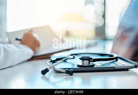 A medical stethoscope lying on a laptop in a doctors office. Hand of a medical professional writing notes in a diary, planning and setting a schedule Stock Photo