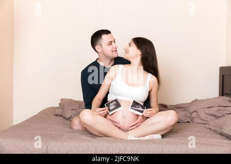 Portrait of young happy married couple hold ultrasound picture. Diverse man and pregnant woman show sonogram image on kid child, excited for parenthoo Stock Photo