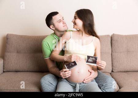 Portrait of young happy married couple hold ultrasound picture. Diverse man and pregnant woman show sonogram image on kid child, excited for parenthoo Stock Photo