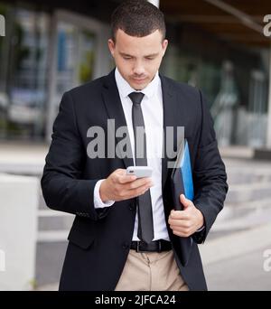 A handsome young mixed race business man using his cellphone while walking through the city on his way to work. Young and confident corporate Stock Photo
