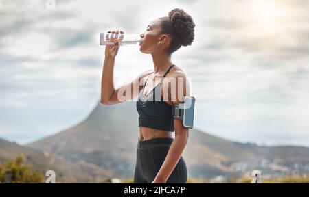 One young african american woman taking a break to drink some water while exercising outdoors. A beautiful and fit mixed race female athlete drinking Stock Photo