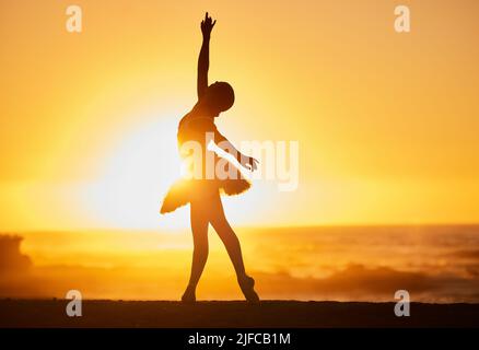 Silhouette of a young ballet dancer on the beach at sunset. Graceful slender ballerina dancing with passion and stretching out her hand Stock Photo