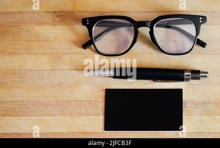 . Above still life flat lay shot of glasses, spectacles, eyewear, a pen and a notepad, notebook on a wooden table, desk in a bright, modern corporate Stock Photo