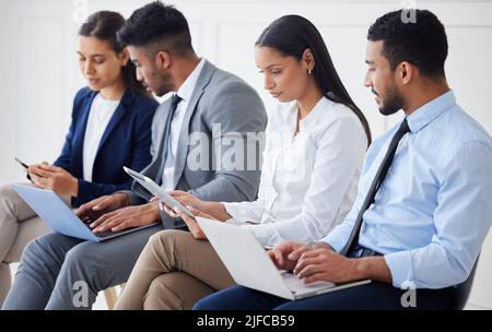 Group of diverse businesspeople waiting for interview and using technology. Team of young applicants sitting together. Professional candidates in line Stock Photo
