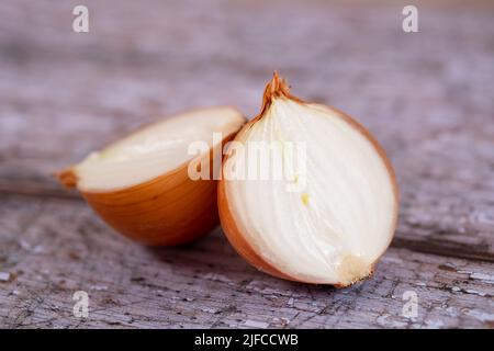 A halved white onion with skin on, against a wooden table top surface background. Stock Photo