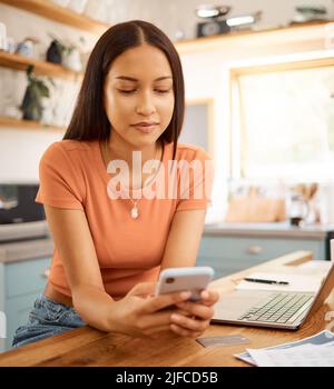 Young beautiful happy mixed race businesswoman holding and using a phone while working from home. One content hispanic woman using social media on her Stock Photo