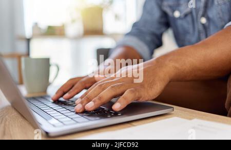 Closeup of a mans hand typing an email while working on a laptop alone at home. One person using a laptop on a table in the lounge at home Stock Photo