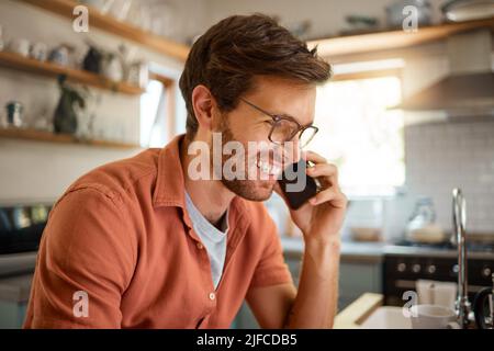 Young content caucasian businessman wearing glasses on a call using a phone while working at home alone. One happy male businessperson smiling and Stock Photo