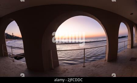 Beach tidal swimming pool through building arches early morning sunrise over the ocean horizon. Stock Photo