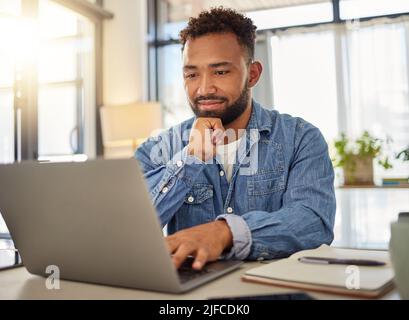 Happy businessman working on his laptop at home. Handsome businessman reading an email on his laptop at home. Freelance entrepreneur typing on his Stock Photo