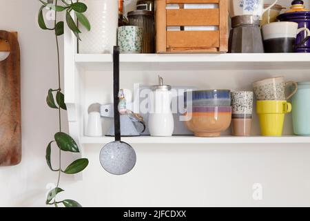 Vintage style kitchen wooden shelf with kitchen utensils. Storage open cupboard, ceramic crockery stand on a shelf in the kitchen. Set of colourful di Stock Photo