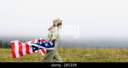 Beautiful child girl in hat with the American flag on foggy mountains. Independence Day of United States USA on 4th of July with family. Freedom. Amer Stock Photo