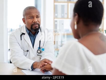 Serious gp in a consult with a patient. African american doctor talking to a patient in a checkup. Woman getting support from her doctor during a Stock Photo