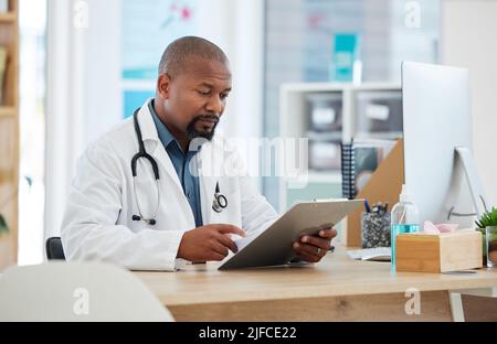 Mature african american doctor checking a patients chart. Focused gp reading a chart on a clipboard. Serious doctor reading a patients report Stock Photo