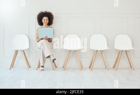 Young woman with afro using laptop while sitting and waiting in line on a chair for interview. Candidate browsing online to prepare for job vacancy Stock Photo