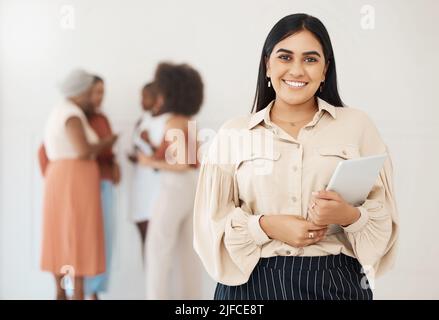 Portrait of a young happy mixed race businesswoman holding a digital tablet in an office at work. Joyful hispanic businessperson smiling while holding Stock Photo