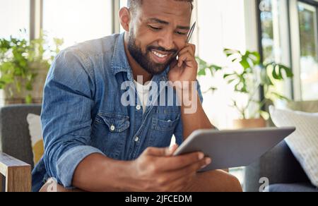 Handsome bachelor using a stylus to write on his digital tablet. Happy young man using his wireless digital device. Man relaxing at home reading an Stock Photo
