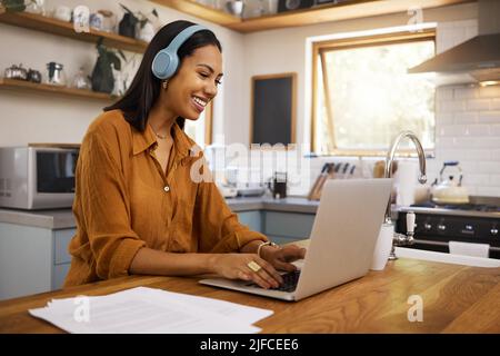 Young cheerful mixed race businesswoman going through paper and bills while typing on a laptop at home. Cheerful hispanic female businessperson typing Stock Photo