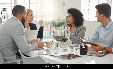 Young mixed race businesswoman with a curly afro explaining an idea in a meeting at work. Group of businesspeople having a meeting together at a table Stock Photo