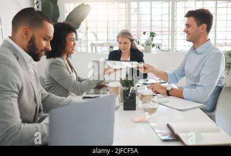 Young happy mixed race businesswoman giving a report to a male caucasian colleague while in a meeting together at work. Businessman smiling while Stock Photo