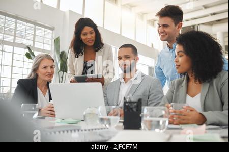 Happy diverse group of businesspeople having a meeting while standing together at a table at work. Business professionals talking and planning while Stock Photo