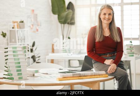 Portrait of leading businesswoman sitting on her desk. Mature businesswoman in her design agency. Creative entrepreneur working in her architecture Stock Photo