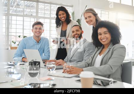 Diverse group of businesspeople having a meeting together at a table at work. Business professionals talking and planning while using technology in an Stock Photo